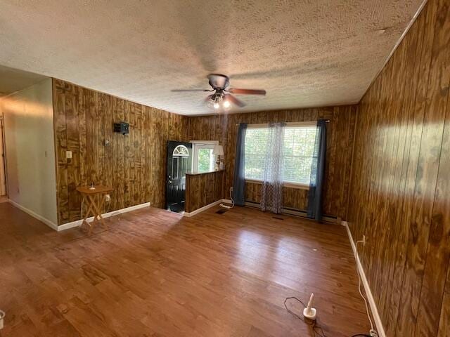 empty room with a textured ceiling, ceiling fan, wood walls, and hardwood / wood-style flooring