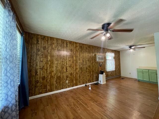 empty room with a textured ceiling, ceiling fan, wood walls, and hardwood / wood-style floors