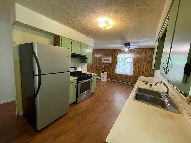 kitchen with green cabinetry, wooden walls, appliances with stainless steel finishes, sink, and ceiling fan