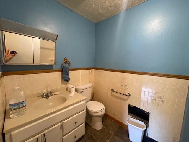 bathroom with toilet, vanity, a textured ceiling, backsplash, and tile walls