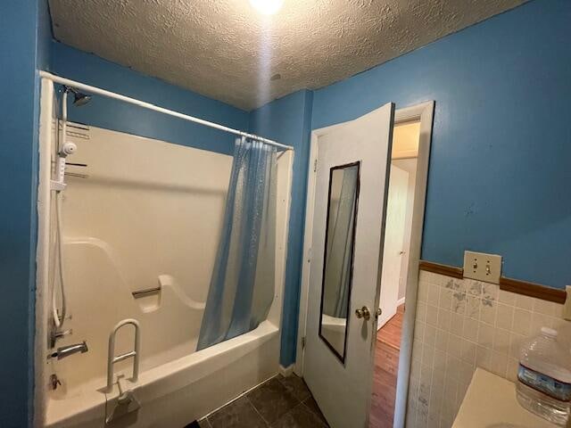 bathroom with tile walls, a textured ceiling, shower / bath combination with curtain, and wood-type flooring