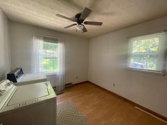 clothes washing area with a textured ceiling, light hardwood / wood-style flooring, baseboard heating, washing machine and dryer, and ceiling fan