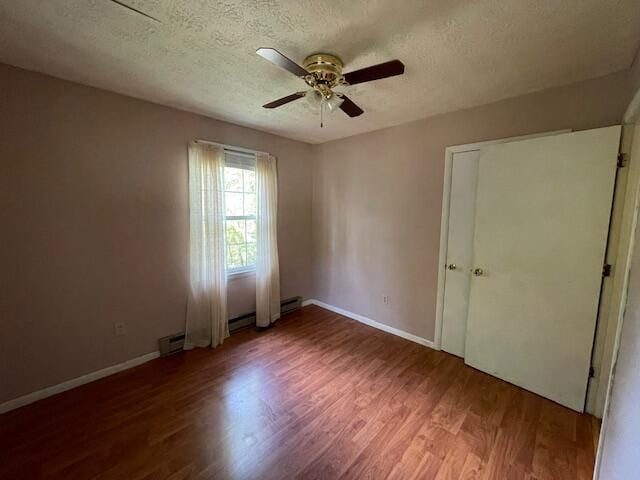 unfurnished bedroom featuring a textured ceiling, ceiling fan, a baseboard heating unit, and hardwood / wood-style floors