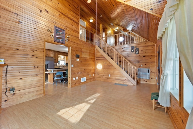 unfurnished living room featuring light wood finished floors, wooden walls, visible vents, stairway, and wooden ceiling