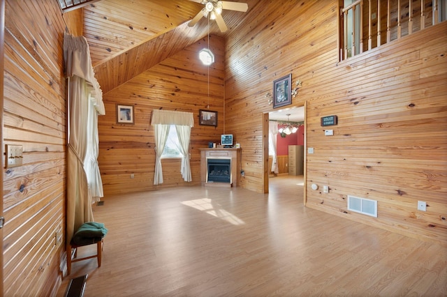 unfurnished living room featuring visible vents, ceiling fan with notable chandelier, wood finished floors, wooden walls, and a fireplace