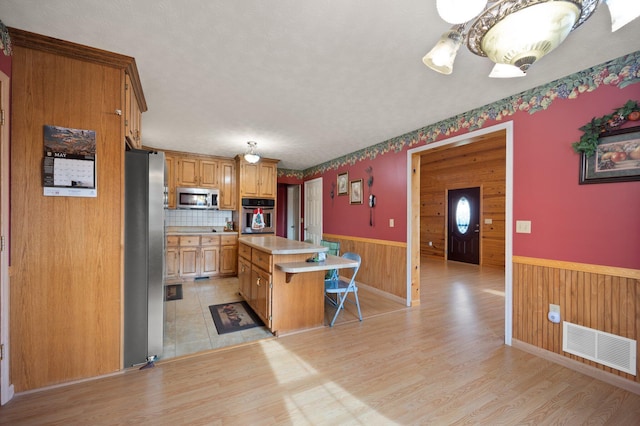 kitchen with light wood-type flooring, a center island, stainless steel appliances, and wooden walls