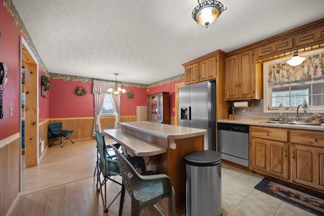 kitchen with a center island, a wainscoted wall, light countertops, appliances with stainless steel finishes, and a sink