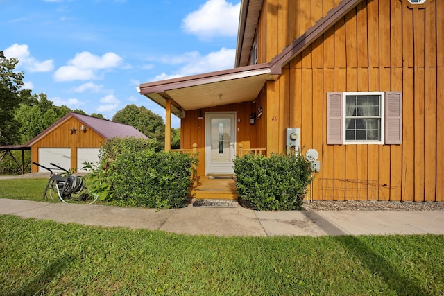 property entrance with board and batten siding, a detached garage, and a yard