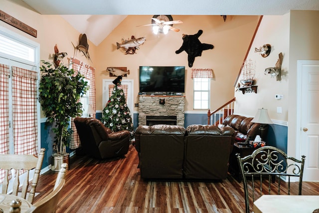 living room with dark wood-type flooring, ceiling fan, vaulted ceiling, and a stone fireplace