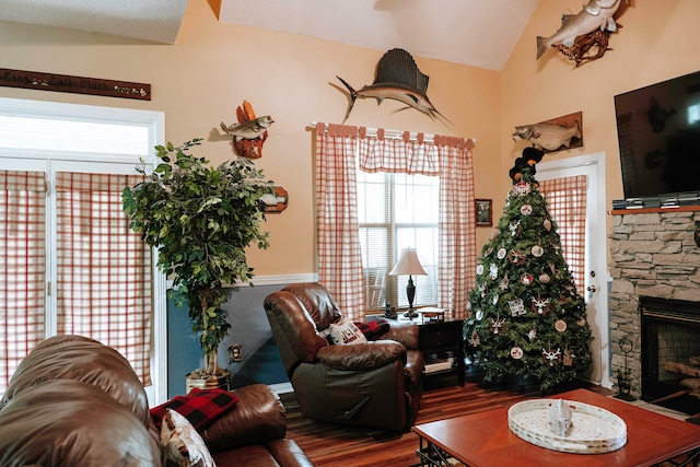 living room featuring vaulted ceiling, hardwood / wood-style floors, and a stone fireplace