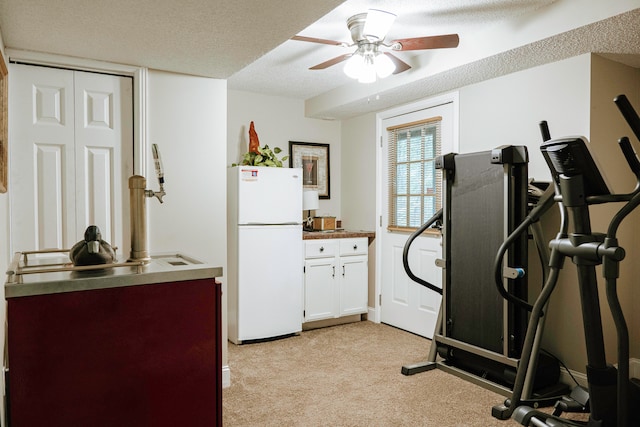 workout area with a textured ceiling, light colored carpet, and ceiling fan