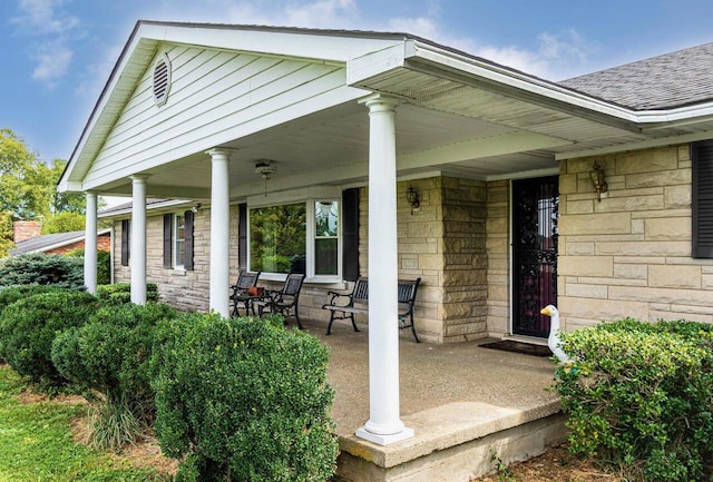 view of exterior entry with stone siding, covered porch, and a shingled roof