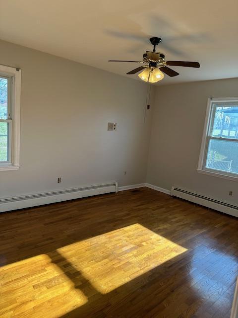 empty room featuring ceiling fan, dark hardwood / wood-style flooring, and a baseboard heating unit