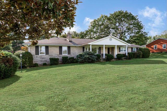 ranch-style house with a front yard, a porch, stone siding, and a chimney