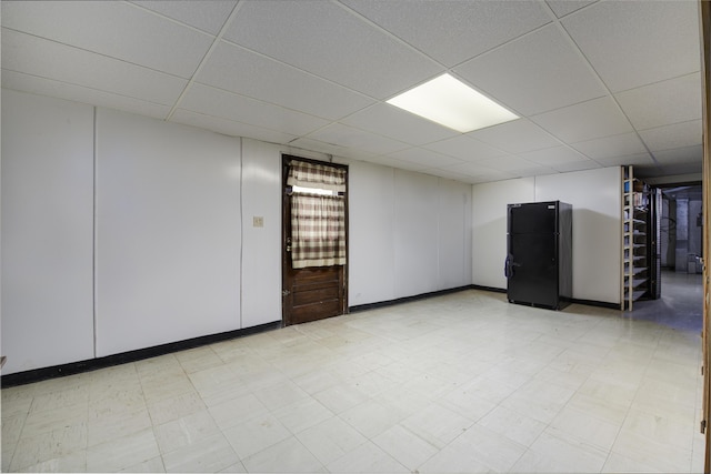 finished below grade area featuring a paneled ceiling, light floors, and freestanding refrigerator