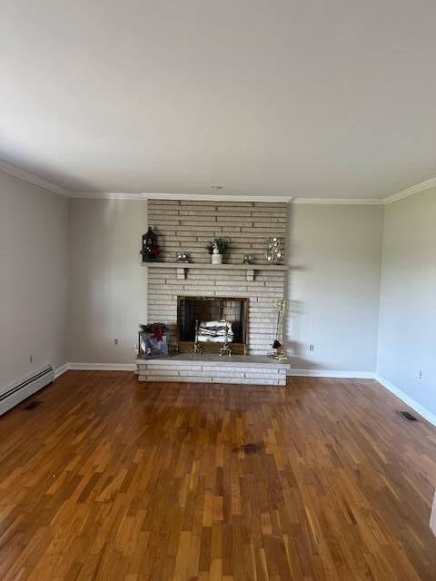 unfurnished living room with baseboards, a brick fireplace, wood finished floors, and crown molding