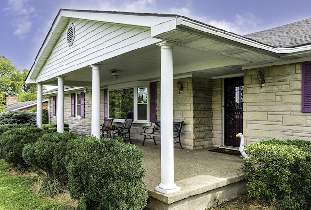 property entrance featuring covered porch, stone siding, and a shingled roof