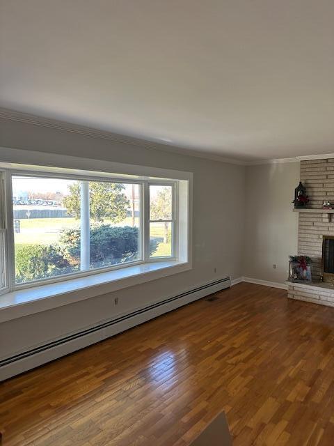 unfurnished living room featuring a baseboard heating unit, wood finished floors, a fireplace, and ornamental molding