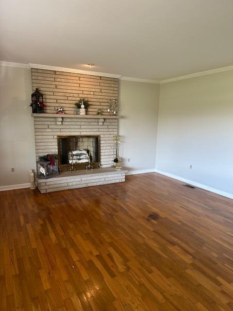 unfurnished living room with baseboards, wood finished floors, a fireplace, and crown molding