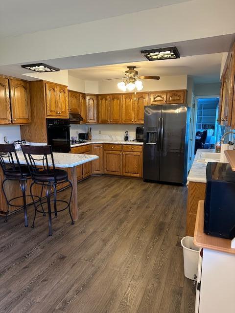 kitchen with brown cabinetry, black appliances, light countertops, and a sink