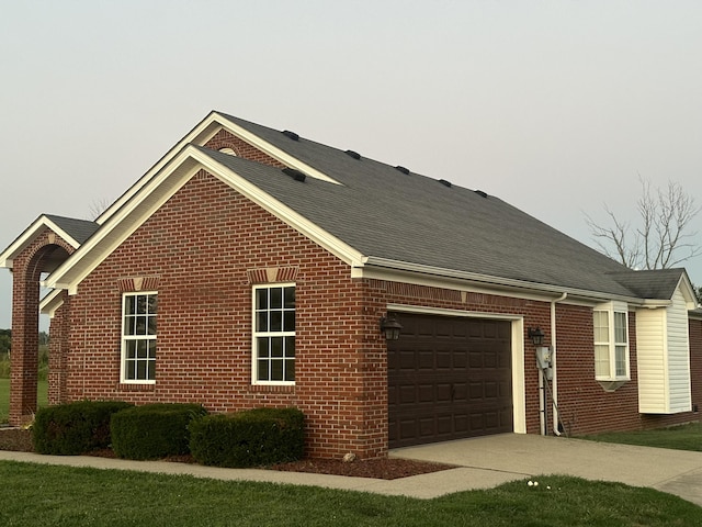 view of home's exterior featuring brick siding, a shingled roof, an attached garage, and concrete driveway