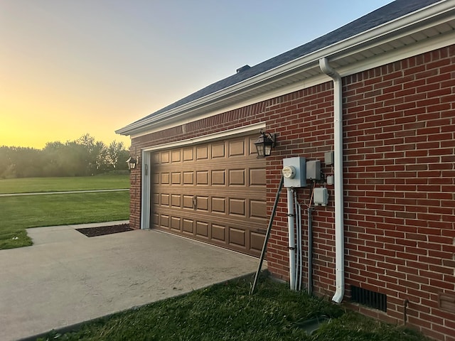 garage at dusk featuring a lawn