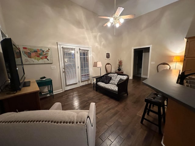 living room with a towering ceiling, ceiling fan, and dark wood-type flooring