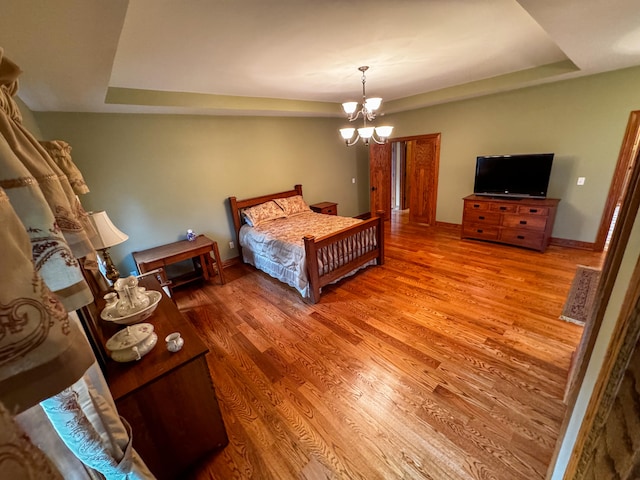 bedroom featuring a raised ceiling, hardwood / wood-style flooring, and a chandelier