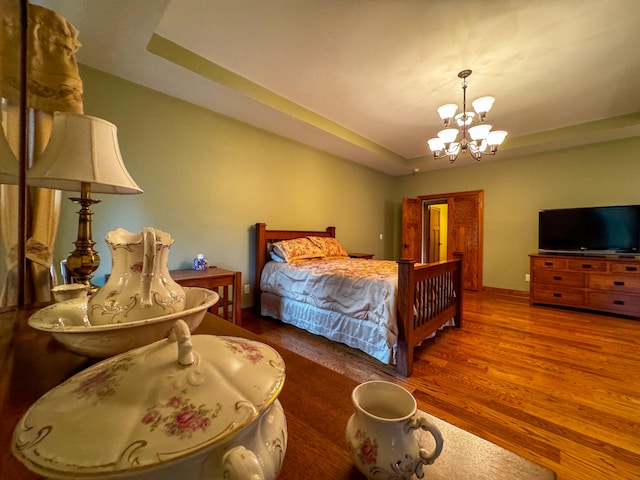 bedroom with hardwood / wood-style floors, a tray ceiling, and a chandelier