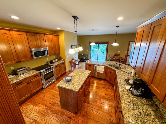 kitchen with decorative light fixtures, appliances with stainless steel finishes, hardwood / wood-style flooring, and a kitchen island