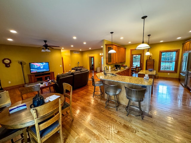 kitchen with a kitchen bar, kitchen peninsula, sink, ceiling fan, and light hardwood / wood-style floors