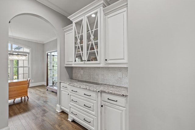 kitchen with ornamental molding, glass insert cabinets, dark wood finished floors, arched walkways, and decorative backsplash
