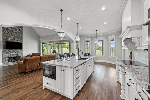 kitchen featuring sink, black appliances, dark hardwood / wood-style floors, an island with sink, and a stone fireplace