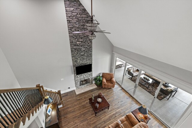 living room with high vaulted ceiling, ceiling fan, a stone fireplace, and wood-type flooring