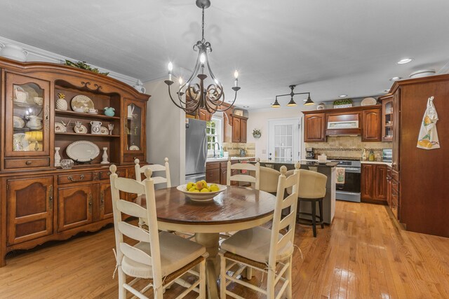 dining room featuring light wood-type flooring, ornamental molding, sink, and a chandelier