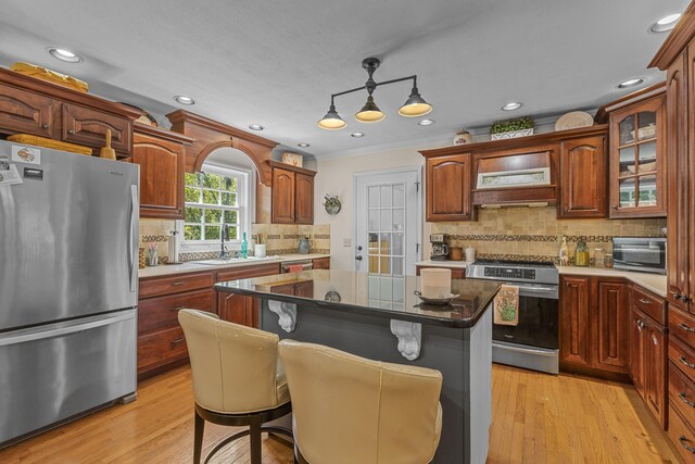 kitchen with a kitchen breakfast bar, hanging light fixtures, stainless steel appliances, light wood-type flooring, and a center island