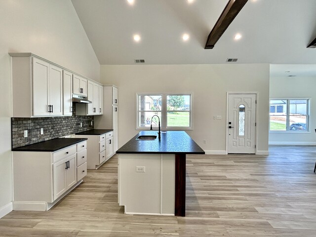 kitchen featuring beamed ceiling, light hardwood / wood-style flooring, an island with sink, sink, and decorative backsplash