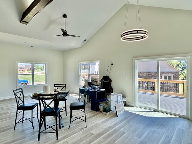 dining space featuring light wood-type flooring, ceiling fan with notable chandelier, high vaulted ceiling, and a healthy amount of sunlight