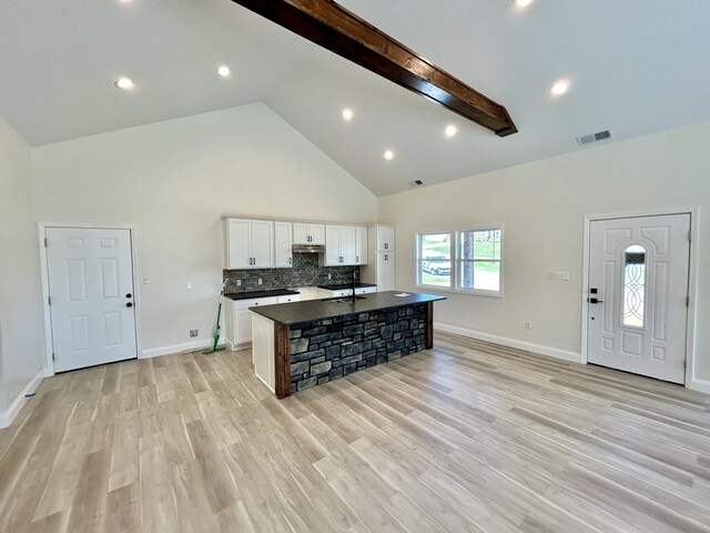 kitchen with beam ceiling, an island with sink, high vaulted ceiling, white cabinetry, and light wood-type flooring