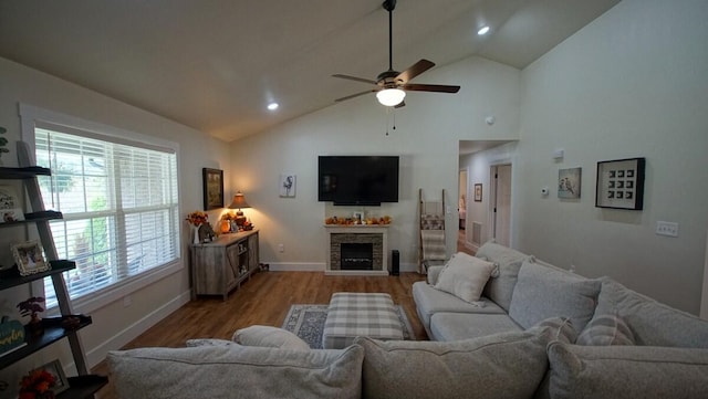 living room with high vaulted ceiling, light wood-type flooring, ceiling fan, and a stone fireplace