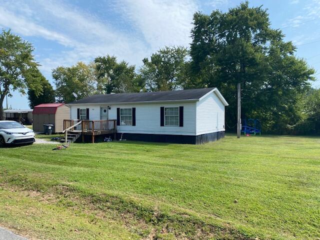 manufactured / mobile home with a shed, a deck, and a front lawn