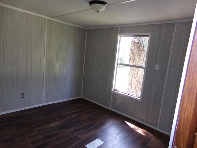 empty room with ornamental molding, wood walls, and dark wood-type flooring