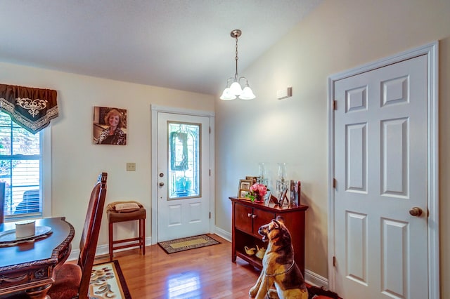 foyer with lofted ceiling, light hardwood / wood-style floors, a healthy amount of sunlight, and a notable chandelier