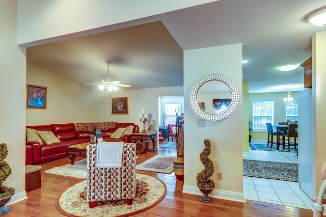 living room with a textured ceiling, ceiling fan, light hardwood / wood-style floors, and vaulted ceiling