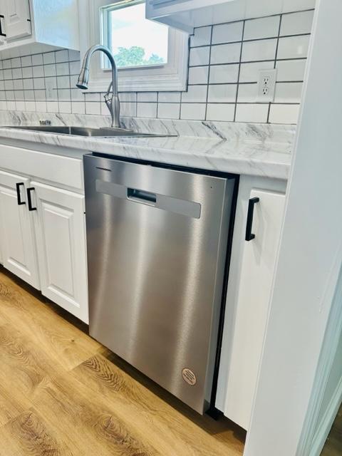 kitchen featuring white cabinetry, backsplash, sink, stainless steel dishwasher, and light hardwood / wood-style floors