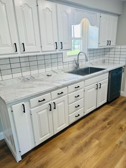 kitchen featuring black dishwasher, light hardwood / wood-style flooring, tasteful backsplash, sink, and white cabinetry