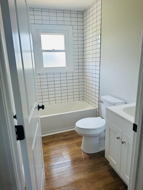 full bathroom featuring tiled shower / bath, vanity, toilet, and hardwood / wood-style floors