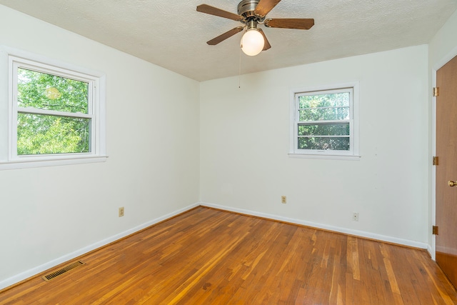 spare room with a wealth of natural light, ceiling fan, wood-type flooring, and a textured ceiling