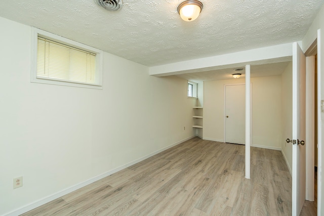 basement with a textured ceiling, a healthy amount of sunlight, and light hardwood / wood-style floors