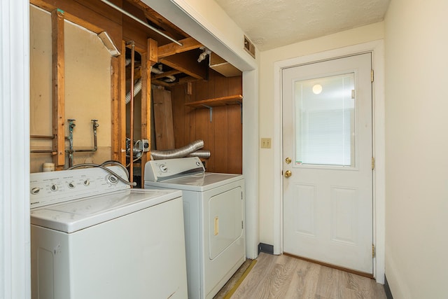 laundry room featuring separate washer and dryer, a textured ceiling, wood walls, and light hardwood / wood-style floors